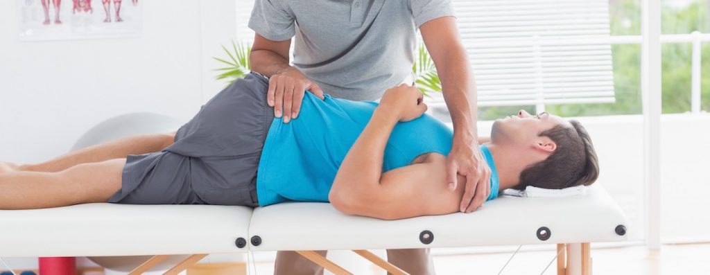 Doctor stretching a young man back in medical office